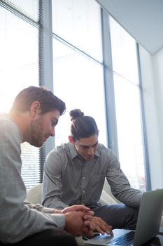 Colleagues discussing over laptop in waiting area of office