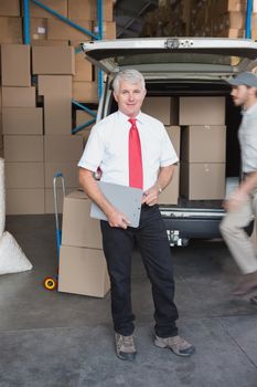 Warehouse manager smiling at camera with delivery in background in a large warehouse