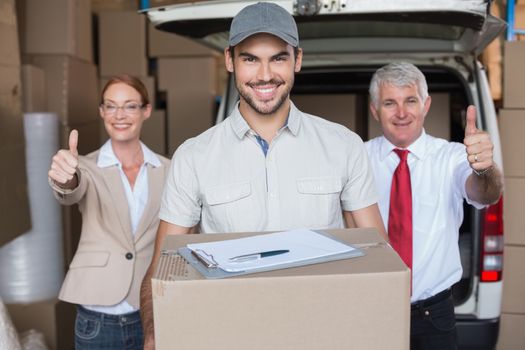 Warehouse managers and delivery driver smiling at camera in a large warehouse