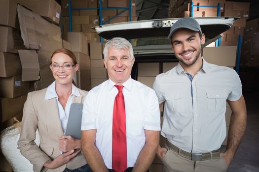 Warehouse managers and delivery driver smiling at camera in a large warehouse