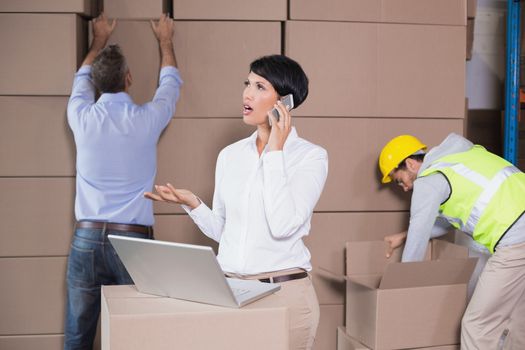 Warehouse manager using laptop and talking on phone in a large warehouse