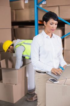 Pretty warehouse manager using laptop in a large warehouse