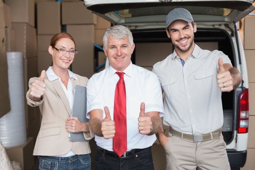 Warehouse managers and delivery driver smiling at camera in a large warehouse