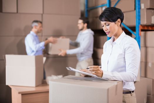 Warehouse manager writing on clipboard in a large warehouse