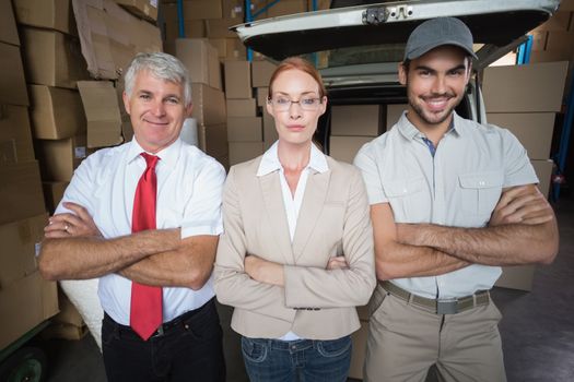 Warehouse managers and delivery driver smiling at camera in a large warehouse