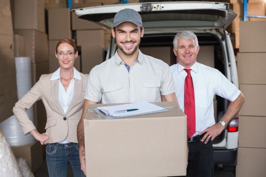 Warehouse managers and delivery driver smiling at camera in a large warehouse