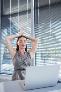 Female executive performing yoga at desk in office
