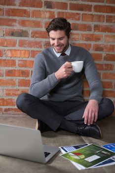 Executive looking at laptop while having cup of coffee in the office 