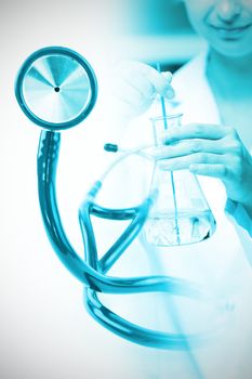 Blue stethoscope  against portrait of a female scientist shaking liquid in an erlenmeyer
