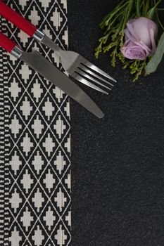 Overhead view of fork and butter knife with rose flower arranged on table cloth