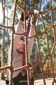 Little girl wearing safety harness climbing rope fence in the forest