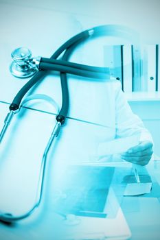 Stethoscope on desk against doctor talking on telephone