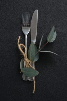 Overhead view of fork, butter knife tied up with leaf on black background