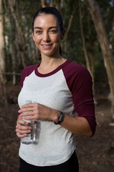 Portrait of woman standing in forest holding water bottle