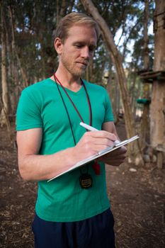 Athletic man taking notes standing in forest during daytime