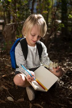 Close-up of little girl with backpack sitting on ground writing in notebook