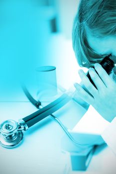Stethoscope on desk against concentrated female scientist looking through a microscope