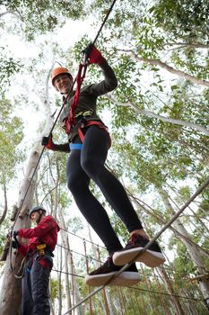 Young smiling woman wearing safety helmet crossing zip line in the forest