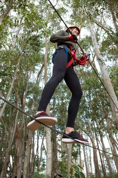 Young smiling woman wearing safety helmet crossing zip line in the forest