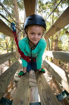 Close-up of little girl wearing helmet trying to cross obstacle in the forest