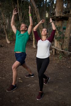 Woman performing stretching exercise with the help of trainer in the forest