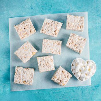 Homemade square bars of Marshmallow and crispy rice and ingredients on blue background. American dessert with marshmallow and crispy rice. Top view. Copy space