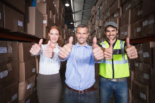 Warehouse team smiling at camera showing thumbs up in a large warehouse