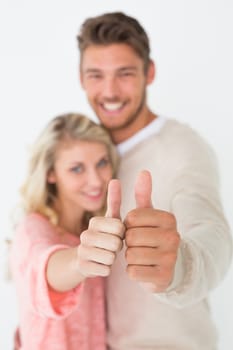 Portrait of happy young couple gesturing thumbs up over white background