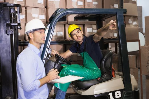 Warehouse manager talking with forklift driver in a large warehouse