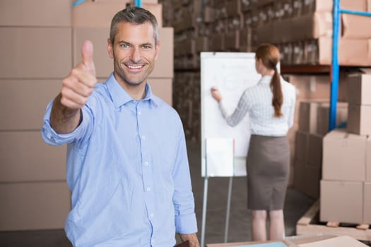 Warehouse manager smiling at camera showing thumbs up in a large warehouse