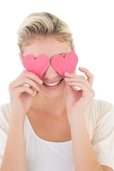 Close up of smiling young woman holding hearts over her eyes against white background