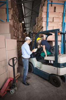 Warehouse manager talking with forklift driver in a large warehouse