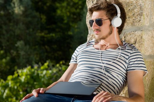 young man relaxing with a tablet pc listening music with headphones, outdoor