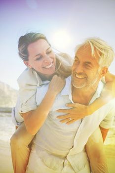 Man giving his smiling wife a piggy back at the beach on a sunny day