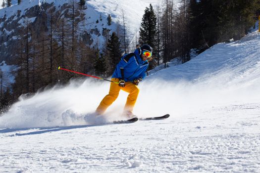 Male skier in blue and yellow clothes on slope with mountains in the background at Cortina d'Ampezzo Faloria skiing resort area Dolomiti Italy