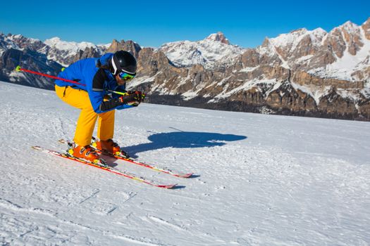 Male skier in blue and yellow clothes on slope with mountains in the background at Cortina d'Ampezzo Faloria skiing resort area Dolomiti Italy