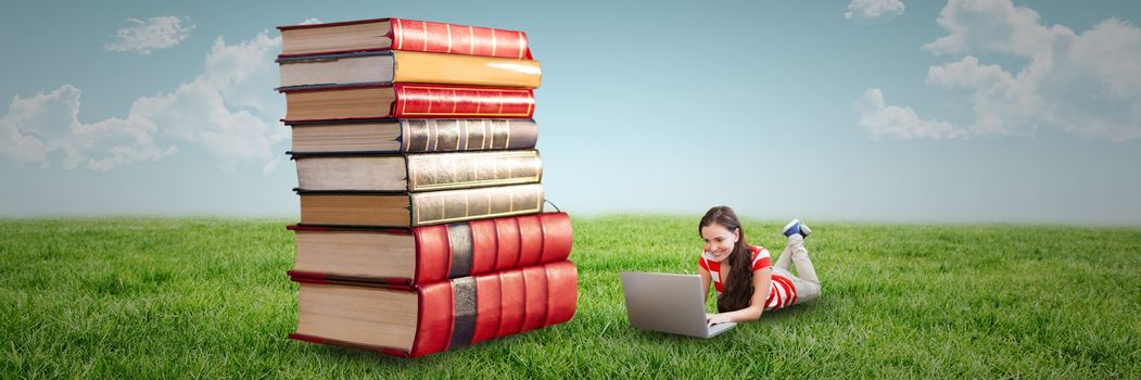 Digital composite of Woman using computer and laying on the floor next to a pile of books outdoors