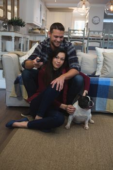 Couple watching television with their pet dog in living room at home