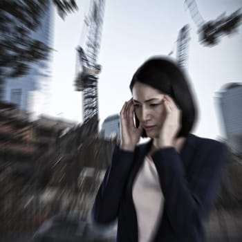 Businesswoman suffering from headache against low angle view of cranes by buildings