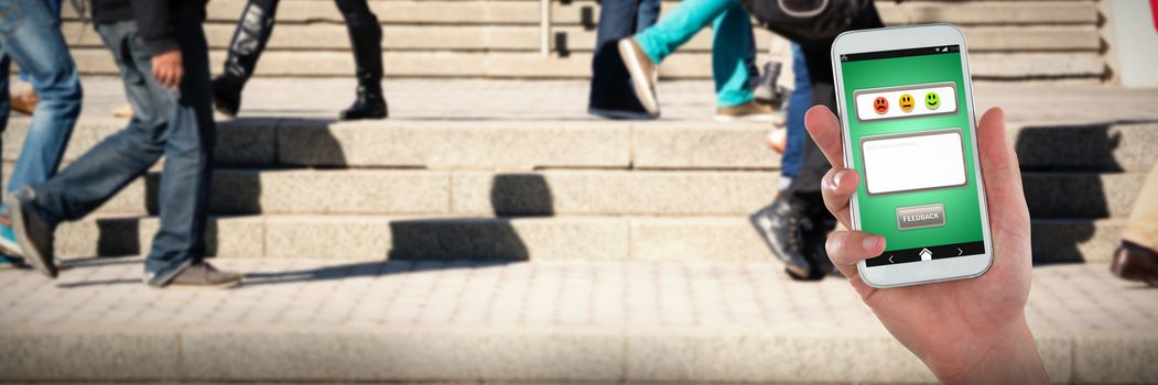 Hand holding mobile phone against people walking on staircase