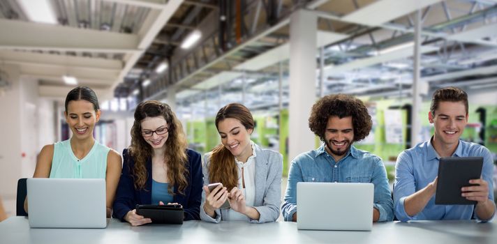 Colleagues using technology while sitting at table against white background against classroom