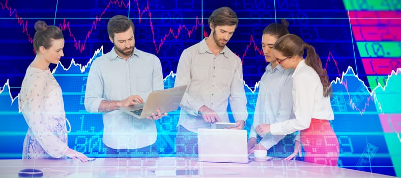 Business people interacting while standing at table against stocks and shares
