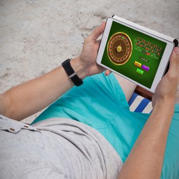Online Roulette Game  against man using digital tablet on the beach