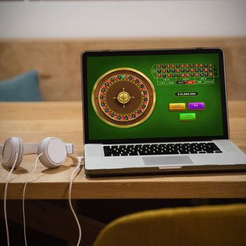 Online Roulette Game  against laptop with headphones and cup on table