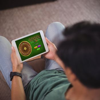 Online Roulette Game  against high angle view of man using digital tablet while sitting on sofa in living room
