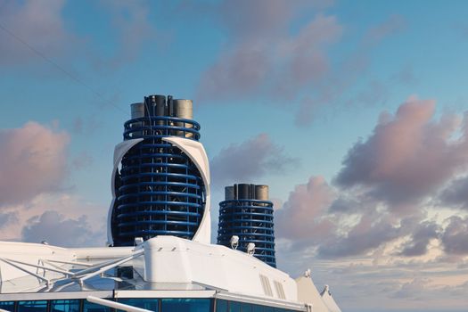 Two blue smokestacks on a white cruise ship under clear blue skies