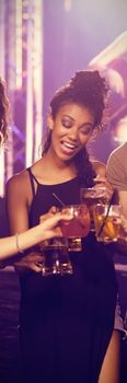 Happy young friends toasting drinks with performer singing in background at nightclub