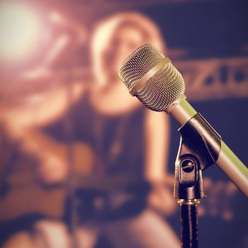 Close-up of microphone  against smiling female guitarist playing guitar at nightclub