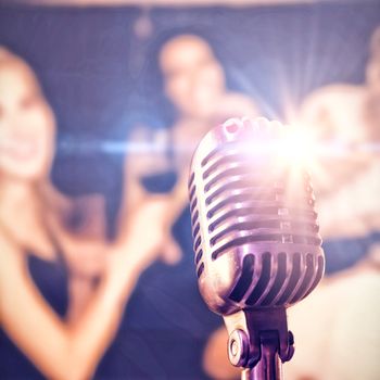 Close-up of microphone  against woman holding wineglass with friends at nightclub