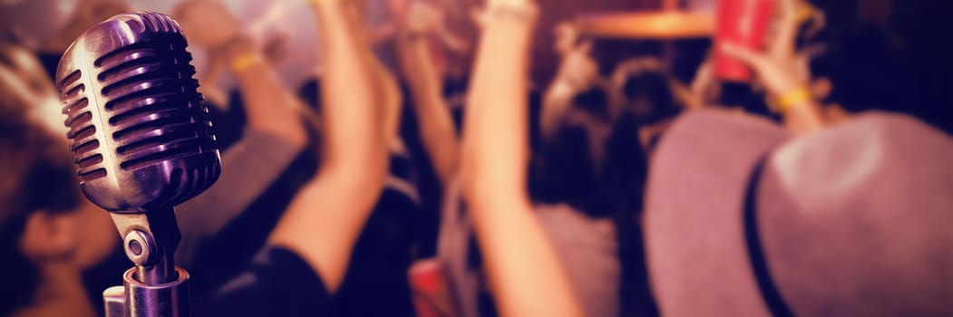 Close-up of microphone  against people with arms raised at nightclub